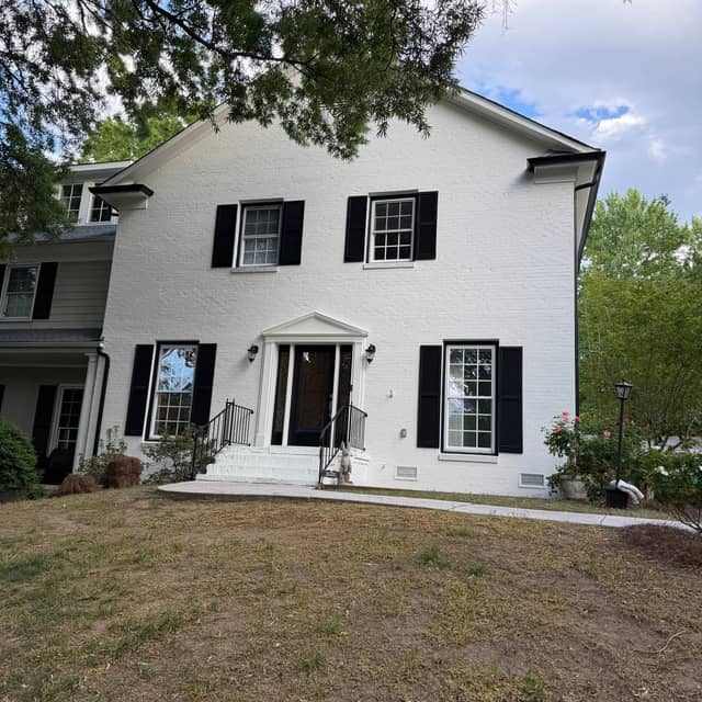 Large white colonial home with black shutters and a columned entry portico after repainting