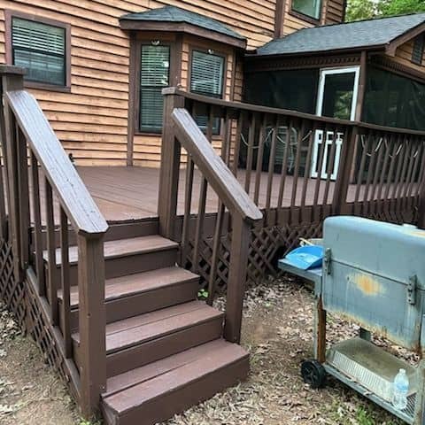 Timber deck, stairs and handrail freshly stained dark brown beneath a screened porch