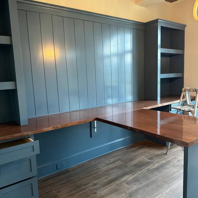 Blue painted built-in cabinetry and panelling wrapping an L-shaped timber desk in a home office