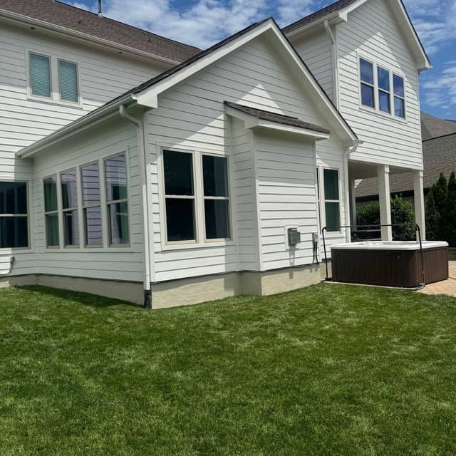 White clapboard home with a covered porch and green lawn after an exterior repaint